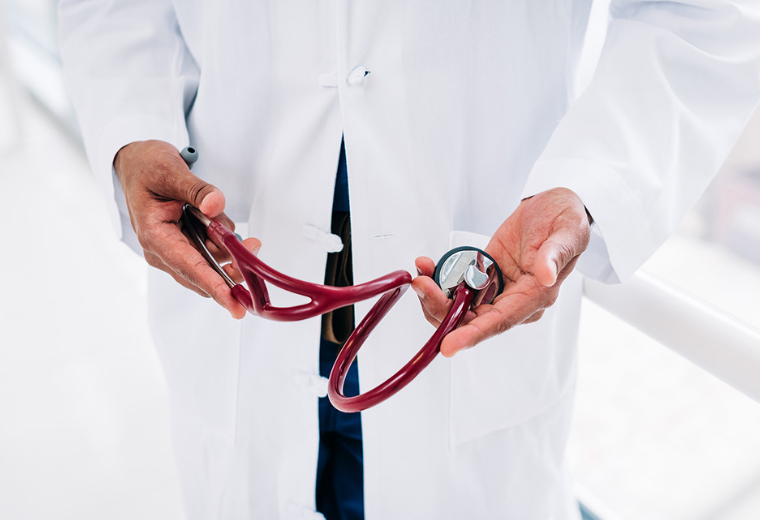 Close-up of a healthcare professional in a white lab coat holding a stethoscope with a dark red tubing.