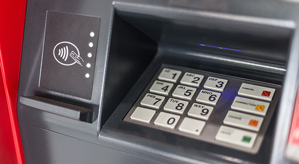 Close-up of an ATM keypad with contactless payment symbol on the left. The keypad has numbered buttons and various colored function keys.