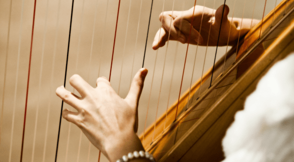 Close-up of hands gracefully playing a harp, fingers poised on strings. The scene conveys a sense of elegance and musical focus.
