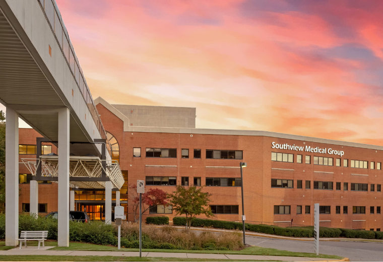 A large brick medical building labeled "Southview Medical Group" under a vibrant sunset sky. The setting is calm, with a walkway and some greenery.