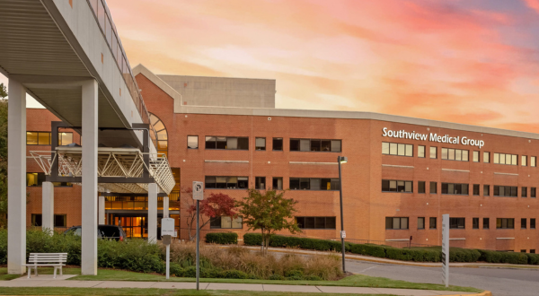A large brick medical building labeled "Southview Medical Group" under a vibrant sunset sky. The setting is calm, with a walkway and some greenery.