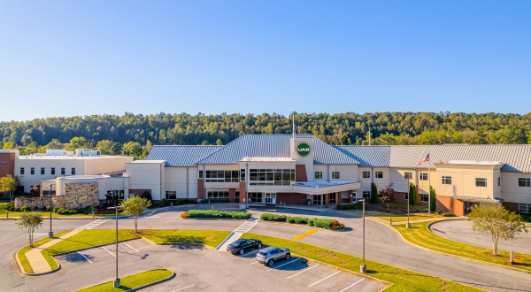 Outside photo of UAB Medicine St. Clair. Aerial view of a modern medical building with a UAB sign, set against a backdrop of lush greenery and clear blue sky, conveying a serene atmosphere.