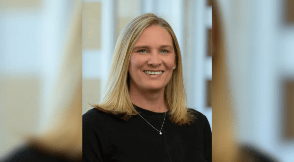 Portrait of Leslie Edwards, CRNP. A smiling woman with shoulder-length blonde hair wearing a black top stands in a softly blurred indoor setting, creating a warm and professional tone.