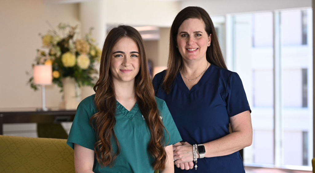Abbey and Tonya Judson, both wearing medical scrubs, smiling together in a brightly lit indoor setting.