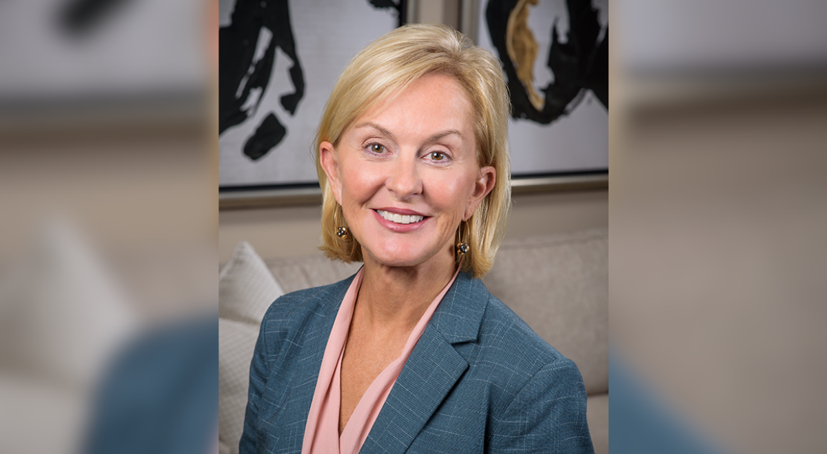 A professional headshot of a smiling woman with blonde hair wearing a blue patterned blazer and a pink blouse.
